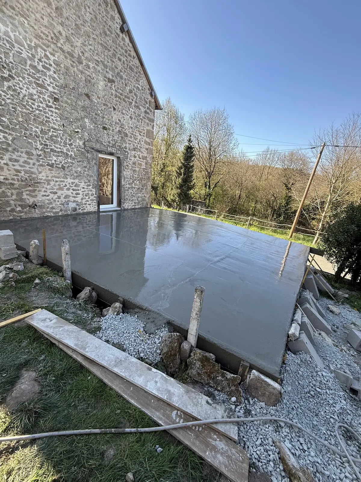 Dalle béton fraîchement coulée contre une maison en pierre, coffrage en bois